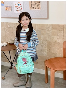 Child wearing a mint green backpack with a teapot monster print in a bright room