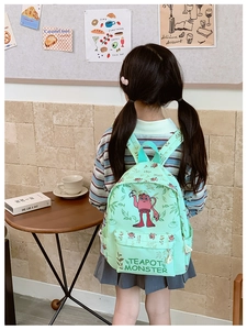 Detail of mint green school backpack with cartoon monster print worn by a child