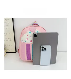 Pink cupcake-themed kids backpack shown next to a tablet for size comparison reference