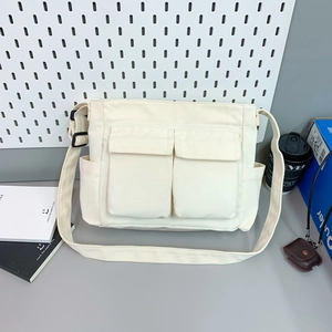Detail of cream canvas messenger bag showing front flap pockets and adjustable black strap