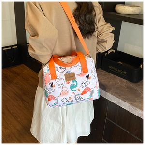 Detail of cute dinosaur print canvas bag with orange straps and leather logo patch