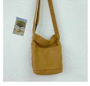 Detail of mustard yellow canvas shoulder bag hanging against a textured white wall