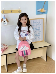 Toddler girl holding a pink sequined cupcake backpack with rainbow straps in a cozy room