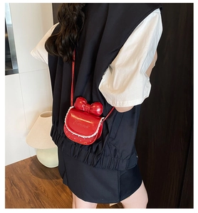 Détail du sac bandoulière rouge avec nœud et dentelle, porté par une fillette