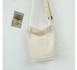 Detail of minimalist cream canvas shoulder bag with adjustable strap and front pocket