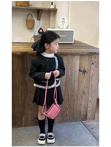 Detail of a pink leather crossbody bag paired with a black pleated skirt for little girls