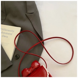 Détail du sac bandoulière nœud rouge avec bordure en dentelle blanche sur veste grise