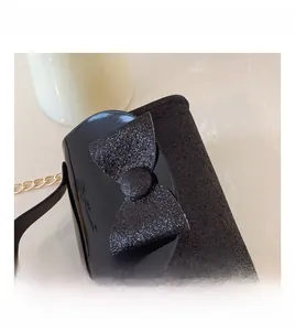 Detail of black patent leather girls handbag with glittery bow and gold chain strap