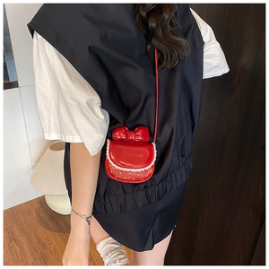 Détail d'un sac à bandoulière rouge avec nœud et dentelle porté par un mannequin