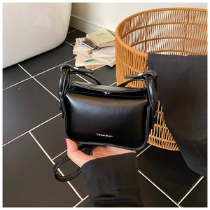 Close-up of small black leather crossbody bag with silver logo and thin shoulder strap