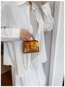 Detail of a shiny orange mini bow handbag with glitter finish and gold chain strap