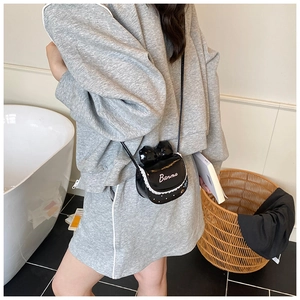 Fillette portant un mini sac bandoulière en cuir verni noir avec nœud en dentelle