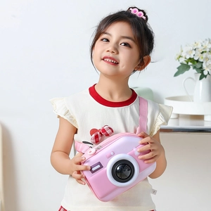 Pink camera-shaped kids crossbody bag with adjustable strap shown in home setting