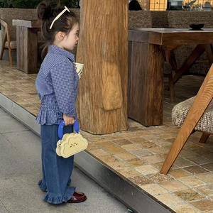 Toddler girl wearing blue plaid shirt and jeans with yellow cloud handbag in a garden setting