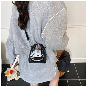 Détail du mini sac bandoulière en cuir verni noir avec charm chiot en peluche sur un mannequin