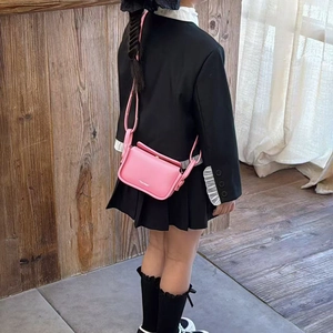 Pink leather mini crossbody bag for kids shown on child model with shoulder strap