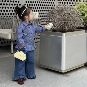 Detail of a child wearing a blue plaid shirt and yellow cloud handbag with chain strap