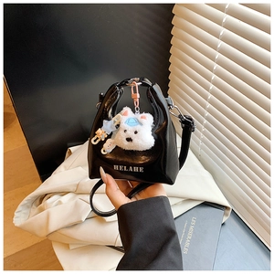 Détail d'un mini sac à main noir brillant avec charm ours en peluche blanc et lettrage