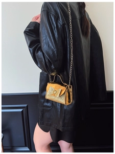 Close-up of a shiny gold sequin bow handbag with an elegant fine metal chain strap