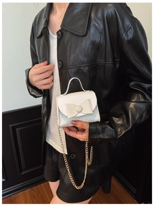 Close-up of white glitter bow handbag for girls with gold chain strap worn with leather jacket