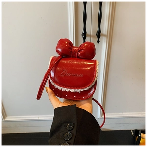 Détail d'un sac à nœud rouge avec dentelle et finition vernie tenu sous une lumière douce