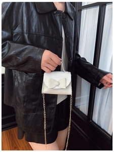 Detail of white glitter mini handbag with bow and gold chain strap on model