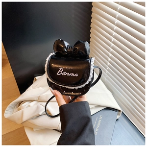 Détail d'un sac bandoulière noir brillant avec nœud, dentelle blanche et texte