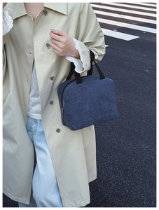 Detail of blue corduroy handbag with black handles on a model in an outdoor setting