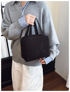 Detail view of a black corduroy handbag featuring vertical textures and a zipper closure