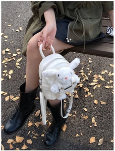 Vue détaillée d'un mini sac à dos blanc avec lapin en peluche sur un banc extérieur