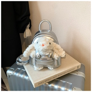 Détail du mini sac à dos argenté avec poupée lapin en peluche posé sur un livre