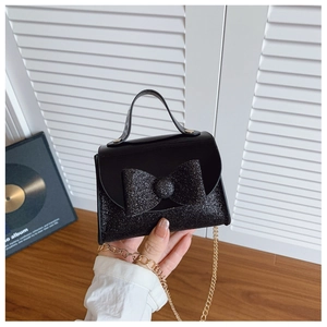 Detailed shot of kids' shiny black glitter handbag with a large bow and gold chain strap