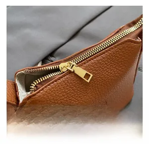 Macro view of brown lychee grain leather texture and glossy gold metal zipper detail