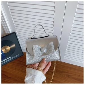 Detailed view of silver sequin mini handbag with large bow and gold metal chain strap