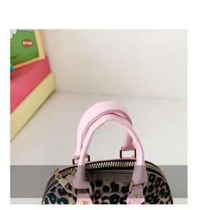 Detail of pink leather handle and golden hardware on leopard print mini shell bag