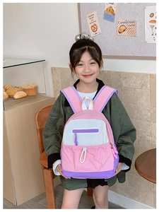 Pink and purple contrast school backpack worn by a girl in a cozy cafe setting