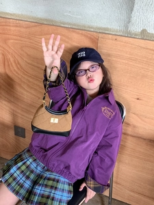 Detail of a brown quilted chain bag held by a child wearing a purple cotton jacket