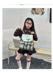 Outdoor shot of a mint green and plaid bow backpack for kids shown on a model