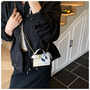 Detailed view of mini white leather child's handbag with large fur ball and gold chain
