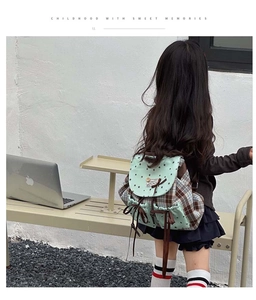 Outdoor lifestyle view of a child wearing a green checkered bow backpack in a cozy setting