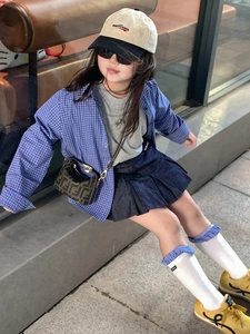Detailed view of child fashion outfit featuring a small crossbody bag with classic pattern