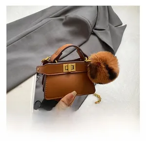 Detailed view of mini brown leather bag with golden chain and leopard print pom-pom charm