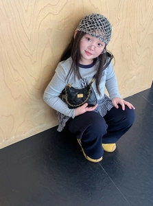 Detailed view of child wearing a black quilted crossbody bag with golden chain and lock