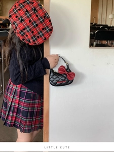 Détail d'un sac bandoulière matelassé noir avec nœud rouge et béret pour enfants