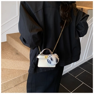 Close-up of a white mini handbag for kids featuring a blue and white fluffy pom-pom charm