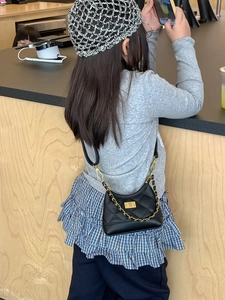 Classic black quilted crossbody bag with gold chain strap shown on a child model