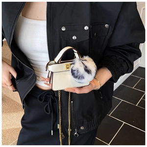 Detailed view of white mini leather handbag with golden twist lock and fluffy pompom