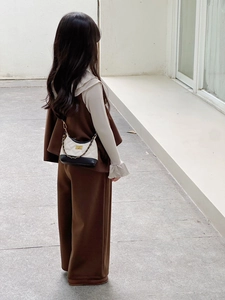 Detail of child wearing a dark coffee vest suit and a quilted chain crossbody bag