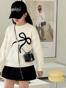 Mädchen mit schwarzer gesteppter Zylinder-Kettentasche mit Strass und Strickpullover