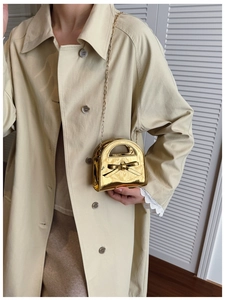 Détail d'un mini sac doré métallisé avec nœud décoratif sur un trench-coat beige
